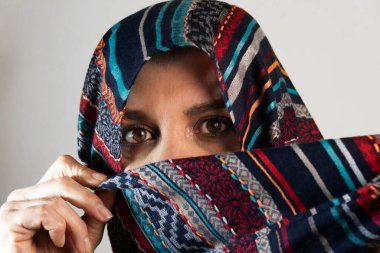 Başörtüsü takan, kameraya bakan, ışık stüdyosunda izole edilmiş bir kadının yakın plan portresi..