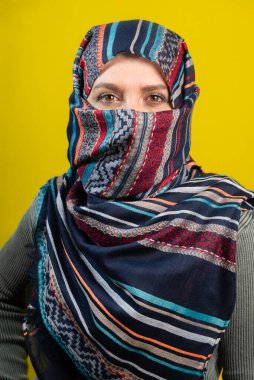 Başörtüsü takan, kameraya bakan, sarı arka planda izole edilmiş bir kadının dikey portresi..