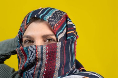 Türbanlı bir kadının portresi, kameraya bakıyor, sarı stüdyo arka planında izole edilmiş..