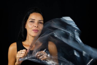 Vücudunun önünde siyah arka planda plastiği olan bir kadın portresi. Ceset ambalajı. Soyut sanat.
