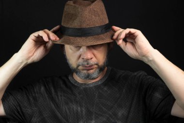 Sakallı adam. İki elinle şapkayı tutarken. Siyah arkaplanda izole.