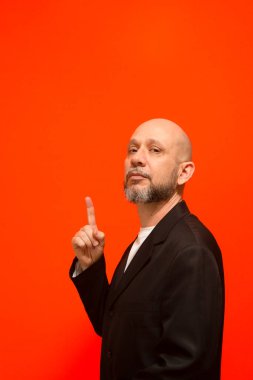 İş adamı, olgun, zarif, parmağını kaldırıyor. Turuncu arka planda izole edilmiş.
