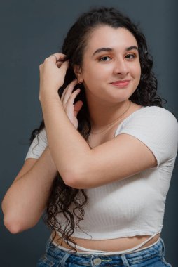 Genç ve güzel bir kadın mutlu bir şekilde gülümsüyor, saçlarına dokunuyor ve kameraya bakıyor. Gençlik kavramı.