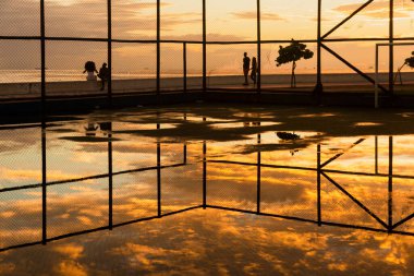 Salvador, Bahia 'daki Rio Vermelho plajında, sarı günbatımına karşı egzersiz yapan insanların silueti..