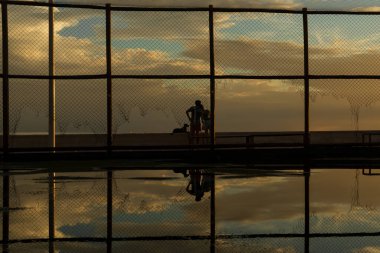 Salvador, Bahia, Brezilya - 05 Aralık 2021: Salvador, Bahia 'daki Rio Vermelho plajında, sarı günbatımına karşı egzersiz yapan insanların silueti.