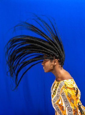 Genç ve güzel bir kadın saçlarıyla hareket ediyor. İzole edilmiş mavi arkaplan.