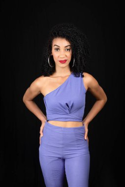 Mavi elbiseli, ciddi, güzel bir genç kadının portresi. Ellerin kalçanda olacak. Kameraya bakıyorum. Stüdyoda siyah arka planda izole edilmiş.