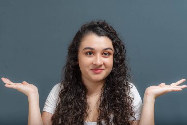 Neşeli genç ve güzel bir kadın kollarında jestlerle neler olduğunu soruyor. Gri arkaplanda izole.