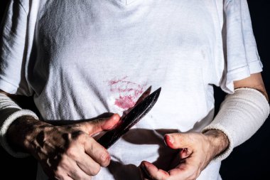 Adam kendine karşı bıçak saldırısı simülasyonu yapıyor. Sahte kan damlalarıyla dolu bir bıçak. Bıçak saldırısı konsepti. Koyu arkaplanda izole.