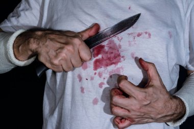 Göğsüne bıçak dayamış bir adam. Sahte kanla lekelenmiş elleri ve gömleği bıçakladı. Bıçak saldırısı konsepti.