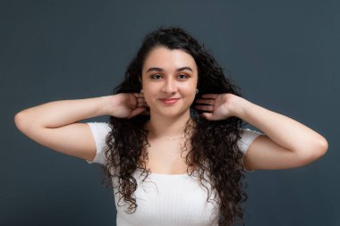 Genç ve güzel bir kadın mutlu bir şekilde gülümsüyor, saçlarına dokunuyor ve kameraya bakıyor. Gençlik kavramı.