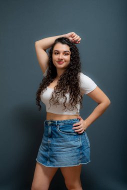 Genç ve güzel bir kadının portresi, elleri başının üstünde, gündelik giysiler giyiyor. Gri arkaplan.