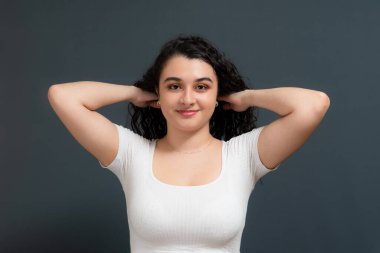 Genç ve güzel bir kadın mutlu bir şekilde gülümsüyor, saçlarına dokunuyor ve kameraya bakıyor. Gençlik kavramı.