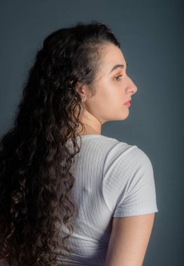 Siyah saçlı, beyaz gömlek giyen güzel bir genç kadın profili. Gri arkaplan. 