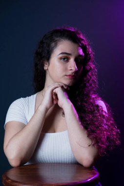 Relaxed and beautiful young woman with hands on chin. Isolated against dark background.