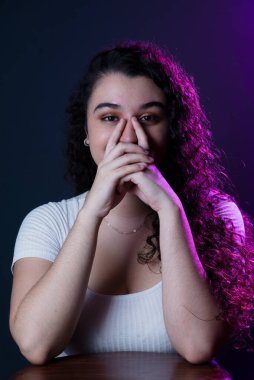 Young beautiful woman with both hands on her lower face. Isolated against dark background.