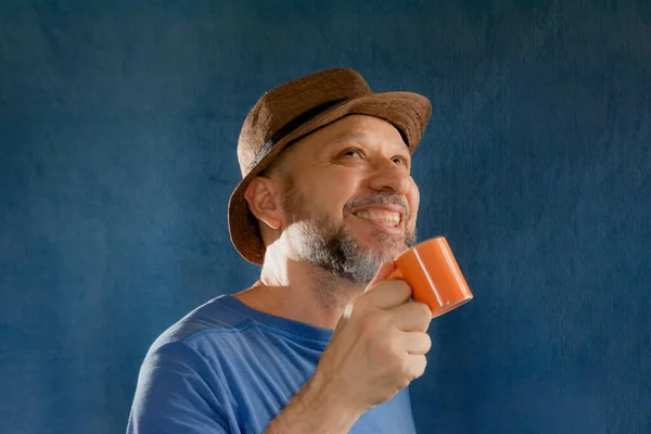 Funny smiling man wearing a hat holding an orange cup. Isolated on blue background