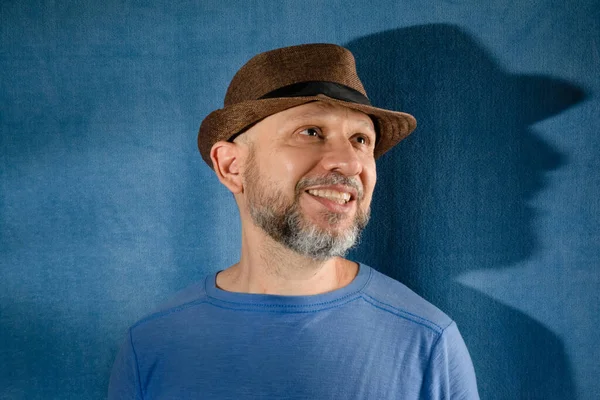 Smiling man wearing hat. Isolated on blue background with shadow.