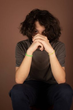 Yakışıklı genç adam, oturuyor, eli yüzü üzerinde. İzole Bisque arkaplanı.