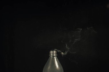 Smoke coming out of a plastic bottle against a black background. Design element. Aromatherapy.