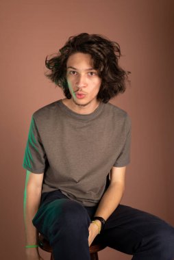 Yakışıklı ve mutlu genç adam oturuyor. İzole Bisque arkaplanı.