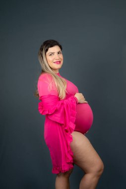 Beautiful pregnant woman standing sideways with hands on belly. Isolated against gray background.