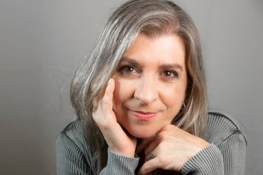 Beautiful, calm woman with her hands on her chin looking at the camera. Isolated on gray background.