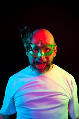 Man portrait, bald, wearing carnival mask and white shirt. Facial expression. Isolated in the black background.