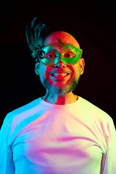 Man portrait, bald, wearing carnival mask and white shirt. Facial expression. Isolated in the black background.