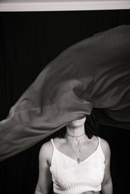 Black and white portrait of woman throwing cloth in the air. Isolated on black background.