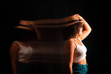 Motion blurred portrait of a woman wearing maron hat against black background.