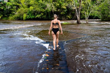 A woman walking on a wooden bridge across the river. City of Valenca, Bahia
