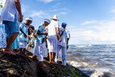 Salvador, Bahia, Brazil - February 02, 2023: Candomble people stand on top of the rocks at Rio Vermelho beach, offering gifts to Yemanja, in Salvador, Bahia.