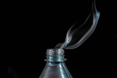 Smoke coming out of a plastic bottle against a black background. Design element. Aromatherapy.