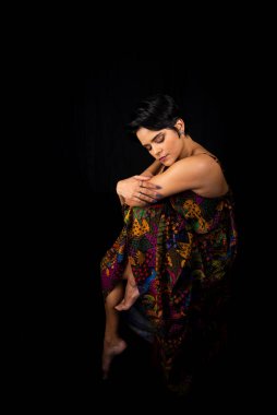 Portrait of young woman sitting on a stool posing for a photo. Isolated on black background.