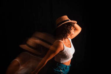 Motion blurred portrait of a woman wearing maron hat against black background.