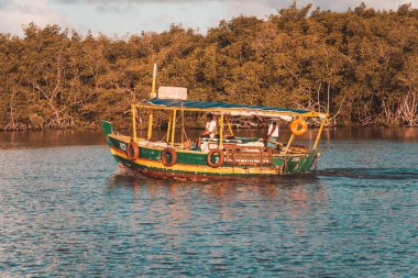 Valenca, Bahia, Brazil - September 09, 2022: Boat sailing on the Una river in the late afternoon while home fishing on the riverbank. City of Valenca, Bahia.