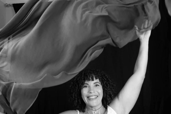 Black and white portrait of woman throwing cloth in the air. Isolated on black background.
