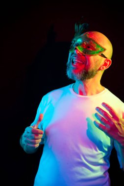 Studio portrait of bald man, bearded, wearing carnival mask. Isolated in the black background.