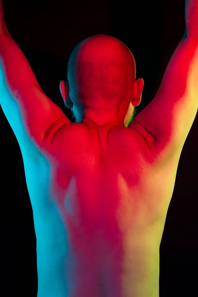 Colorful bald man portrait, shirtless, back to the camera. arms up. Isolated in the black background.