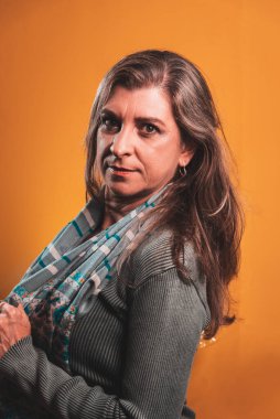 Güzel bir kadın, ciddi ve sakin, boynunda bir atkıyla. Turuncu arka planda izole edilmiş.