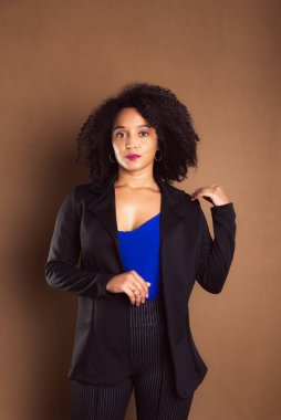Kahverengi arka planda duran siyah ceketli bir kadın. İş kadını. Stüdyo resmi.