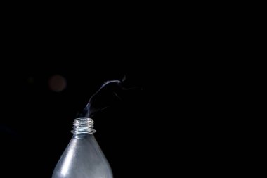 Moving smoke coming out of a plastic bottle. Isolated on black background.