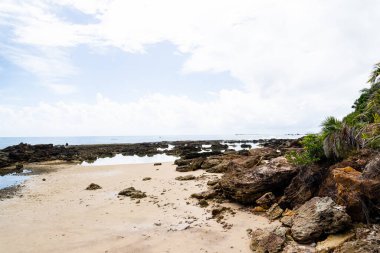 Deniz kenarındaki taş mercanlarla sahilin güzel manzarası. Arka planda bulutlar olan mavi gökyüzü.
