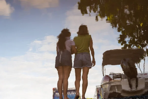 Two women reflected in the puddle of water, embracing. City of Valenca, Bahia.