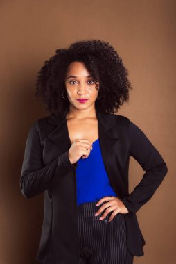 Kahverengi arka planda duran siyah ceketli bir kadın. İş kadını. Stüdyo resmi.