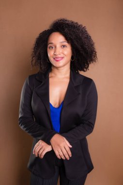 Kahverengi arka planda duran siyah ceketli bir işletmeci kadın. Stüdyo resmi.