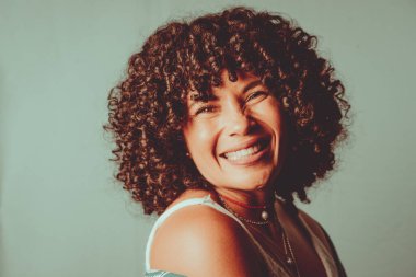 Portrait of cheerful, smiling woman with curly hair. Isolated on light green background.