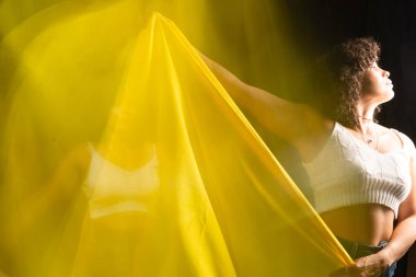 Motion blurred portrait of a woman with yellow cloth against black background.