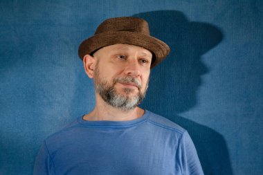 Portrait of a bearded middle-aged man wearing a hat. Isolated on blue background with shadow.